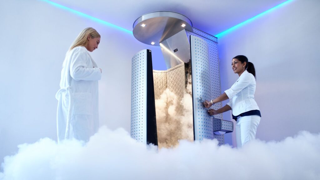 Woman opening the door to a cryotherapy machine while another prepares to step inside.